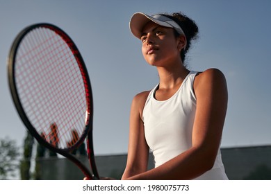 From below young ethnic female athlete with racket looking away while playing tennis on court in summer - Powered by Shutterstock