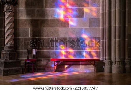 Bench and a chain against the wall in a church with a light pattern through a tainted glass