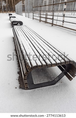 A bench is covered in snow and is empty. The bench is long and has a curved shape