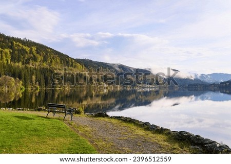Bench infront of the Titisee lake with clouds and reflections in sun light