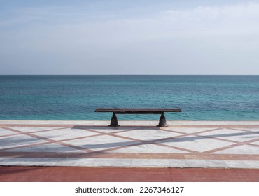 Bench made of wood, standing on a pathway covered in orange tiles. The bench is overlooking a beautiful seaside landscape with no people around.  - Shutterstock ID 2267346127