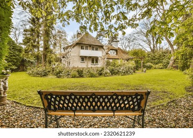 a bench in the middle of a yard with a house in the background and leaves on the ground around it - Powered by Shutterstock