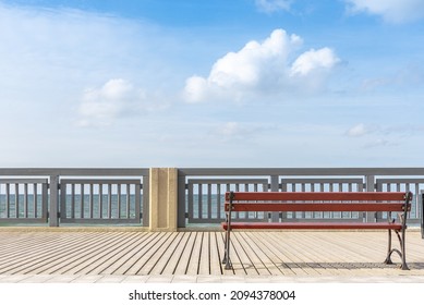 A bench on the sea embankment. An empty simple bench on a wooden sidewalk. A place for tourists to relax and walk. Railings along the embankment.