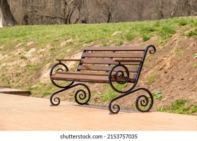 The bench is in the park. Beautiful bench made of wood and metal with graceful rounded lines. Elegant and stylish bench