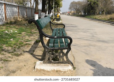 A bench sits on the train platform, quiet and still, waiting for someone to rest. Trees surround the area on both sides, adding shade and a calm, natural feel. The platform feels peaceful, with the sound of leaves moving in the wind and the open space stretching along the tracks. It looks like a simple place where travel slows down for a moment before the next train arrives.