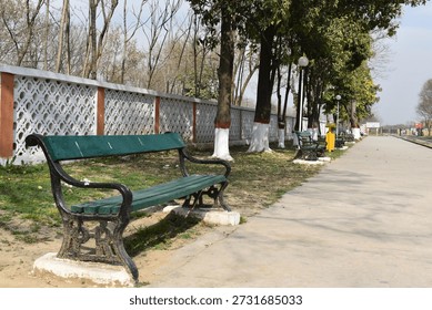 A bench sits on the train platform, quiet and still, waiting for someone to rest. Trees surround the area on both sides, adding shade and a calm, natural feel. The platform feels peaceful, with the sound of leaves moving in the wind and the open space stretching along the tracks. It looks like a simple place where travel slows down for a moment before the next train arrives.