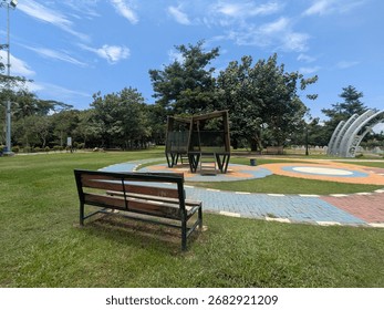 A bench sits in a park with trees and structures under a blue sky.