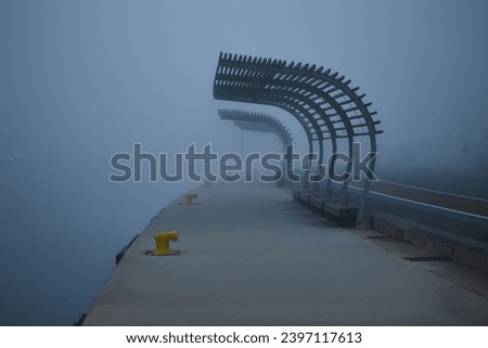 Benches along empty pier during heavy fog. Vague silhouettes in the background.
