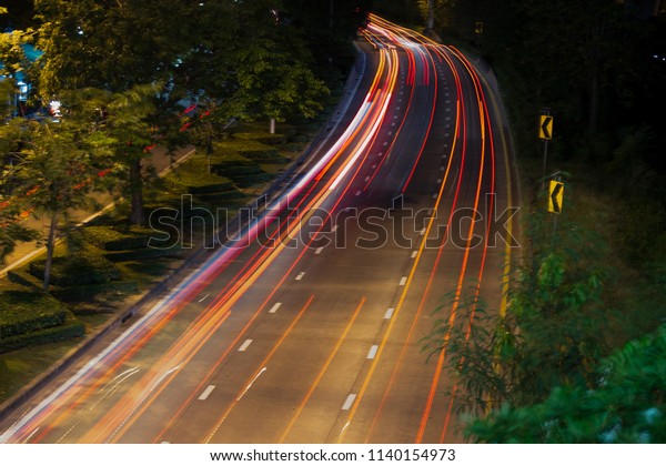 Bend in the road with long
exposure and highway that curves to the right.  Cars coming in both
directions at night, illuminating the roadway with street
lights.