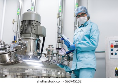 Bended Scientist In Blue Lab Uniform Stand Near Compressors Engine, Tablet In Hands, Look At Camera