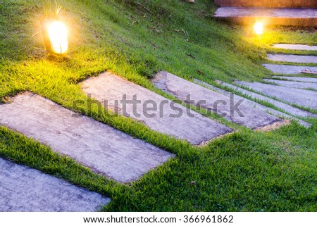 Bending garden stone path at night with glowing light from garden outdoor light

