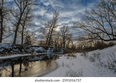 Beneath a cloudy sky, a tranquil river mirrors the fading light surrounded by snow-covered trees and quiet surroundings.