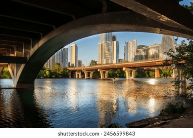 Beneath the North Lamar Bridge in Austin, Texas, the tranquil waters of Lady Bird Lake mirror the golden hues of the cityscape, creating a beautiful reflection on a summer day. - Powered by Shutterstock