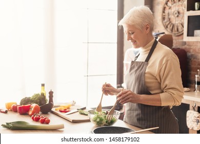 Benefits Of Healthy Nutrition. Positive Senior Lady Cooking Fresh Salad At Kitchen, Empty Space