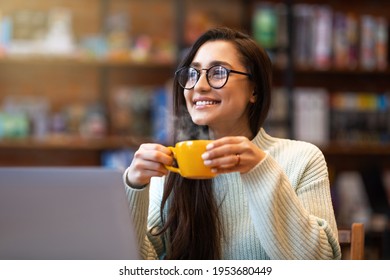 Benefits Of Remote Work. Dreamy Lady Enjoying Coffee During Work On Laptop Computer In City Cafe, Smiling And Looking Aside. Young Freelancer Having Break While Working Online In Internet