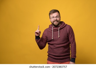 Benevolent, smiling man points finger up, he has an idea and he is glad about it. Copy space. Yellow background. - Shutterstock ID 2072383757