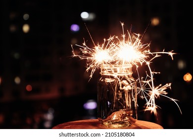 Bengal lights in glass jar against background of  busy night city. Festive sparklers at night.