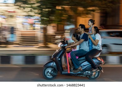 Bengaluru, Karnataka / India - August 02 2019: Grainy motion blur shot of a family of four riding on a scooter without wearing helmet dangerously 