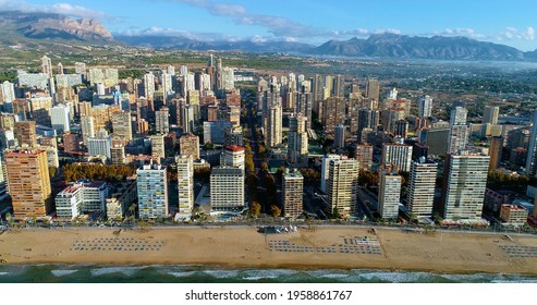 Benidorm city in Spain, with mountains in the background. We can see the coastline, the beach and the buildings of the city near the shore