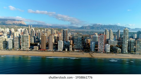 Benidorm city in Spain, with mountains in the background. We can see the coastline, the beach and the buildings of the city near the shore