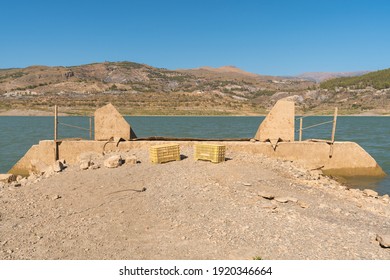 Beninar reservoir between mountains in southern Spain, there are two metal railings, there are 2 plastic boxes, there are mountains with vegetation and the sky is clear