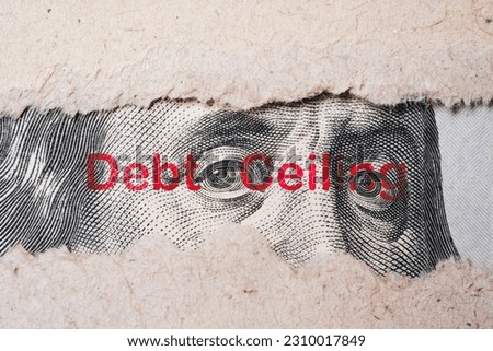 Benjamin Franklin face from USD dollar banknote behind of torn paper with debt wording for America's public debt is high and the debt ceiling needs to be raised concept.