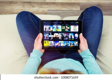Benon, France - January 21, 2018: woman sitting cross-legged on her couch and using her touch pad to connect to watch films on the Amazon prime video app. 