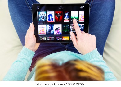 Benon, France - January 21, 2018: woman sitting cross-legged on her couch and using her touch pad to watch movies on demand on Netflix. 