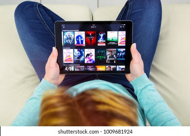 Benon, France - January 21, 2018: Woman Sitting Cross-legged On Her Couch And Using Her Touch Pad To Watch Movies On Demand On Netflix.