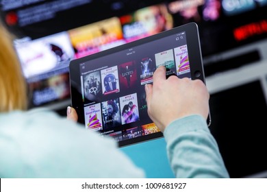 Benon, France - January 21, 2018: Woman Holding a touch pad and switching channels on France Netflix HomePage. with TV set on background. 