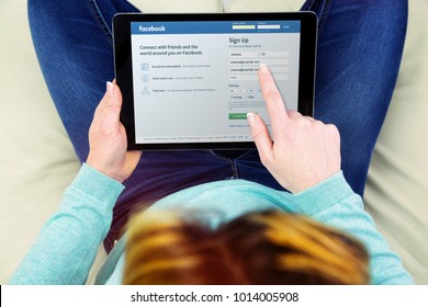 Benon, France - January 21, 2018: woman sitting cross-legged on her couch and using her touch pad to create a new user account on facebook. Facebook is the largest social network in the world.