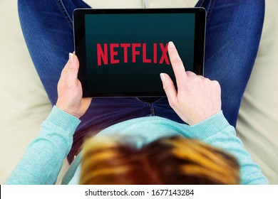 Benon, France - January 21, 2018: woman sitting cross-legged on her couch and using her touch pad to watch movies on demand on Netflix.
