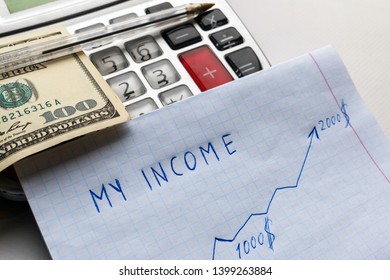 The bent hundred dollar bill and pen lie on a gray calculator, next to them is a paper with the inscription my income and an arrow that shows profit growth. calculation of family income growth - Shutterstock ID 1399263884