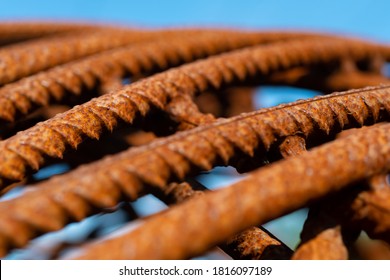 Bent And Rusty Iron Rods Or Steel Reinforcements On A Building Site With Sunlight And Blue Sky, Selective Focus And Vanishing Point. Macro Close Up Of Corroded Metal With Warm Orange Surface Color.