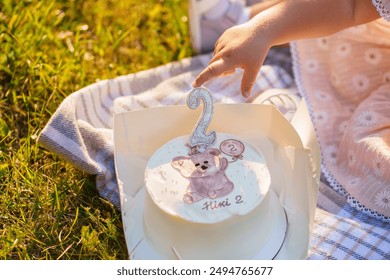 Bento cake for a child's birthday with a candle in the form of the number two, a drawing in the form of a bear cub, the concept of a children's party, the child's hand reaches for the cake - Powered by Shutterstock