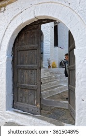 BERAT, ALBANIA - APRIL 12, 2015: A Boy Looks Through The Half Open Traditional Wooden Door Of His House. The Old Town Of Berat Is A Striking Collection Of White Ottoman Houses, Climbing Up The Hill.