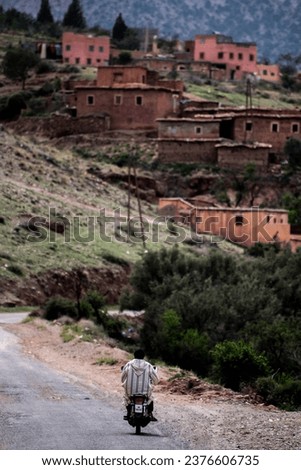 Berber man riding a motorbike through a valley with old traditional houses in the Atlas mountains in Morocco