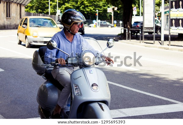 Bergamo/Italy - 7/27/2017: Elderly man\
in a blue suit on a scooter on the road on a sunny day waiting for\
a traffic signal in Bergamo, Italy. Helmet and safety\
first.