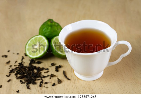 Bergamot tea or Earl Grey\
tea in white cup and fresh bergamot fruit with sliced on brown\
wooden table.