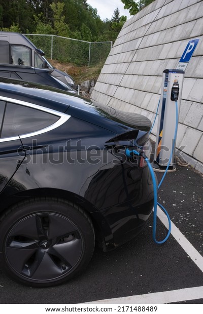 Bergsbygda, Norway - May 25,\
2022: A static shot of a solid black Tesla Model 3 dual motor\
charging at the Recharge AC charging station in a cloudy spring\
day. Selective\
focus.