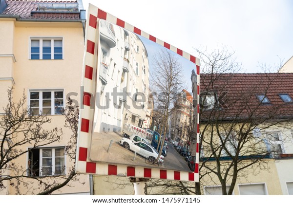 Berlin, Berlin/Germany - 24.03.2019: A traffic\
mirror on a road that helps drivers to drive out of an exit. The\
mirror is framed red-white and in its mirror image you can see a\
street with cars.
