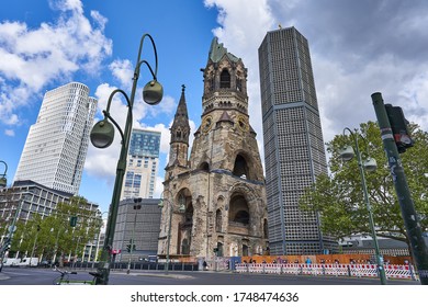 Berlin Germany, 28.05.2020: The Kaiser Wilhelm Memorial Church, In German Kaiser-Wilhelm-Gedächtniskirche, Spring Time In The City, With A Blue Sky And Green Trees On The Road Side