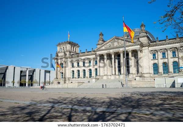 BERLIN, GERMANY April 18, 2020. Shadows at the\
Reichstag building in the government district. The European and\
German flags in the\
wind.