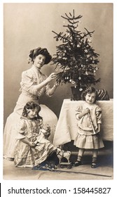 BERLIN, GERMANY - CIRCA 1900: Antique Family Portrait Of Mother And Children With Christmas Tree Wearing Vintage Clothing, Circa 1900 In Berlin, Germany