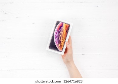 BERLIN, GERMANY - DECEMBER 09, 2018: Woman hands holding the colorful box of the latest Apple iPhone XS smartphone against white wooden background. Unboxing concept with copy space