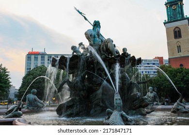 Berlin, Germany - Jul 2010: Bronze statue holding Trident at Neptune fountain in Alexanderplatz with building and St. Mary's Church clock tower and sunset sky background.