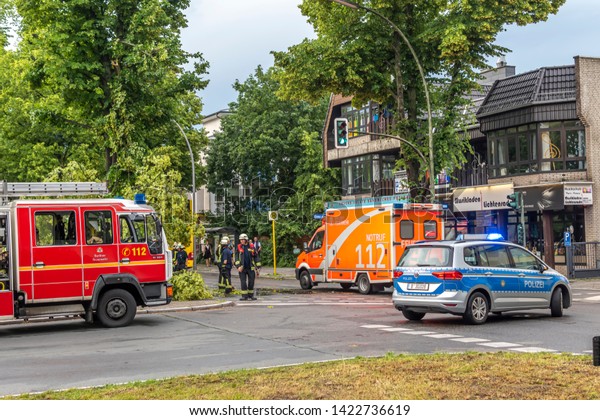 Berlin, Germany - June 12, 2019: An uprooted\
tree lying on a main street in Berlin, Germany, after a heavy\
storm. The police are blocking the road and firefighters are\
clearing away the\
branches.