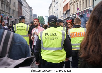 Berlin, Germany - May 1, 2019: Back Turned Policeman Wearing The Yellow Bib Of The Communication Team (German: Kommunikationsteams), Anti-conflict Group Of The German Police