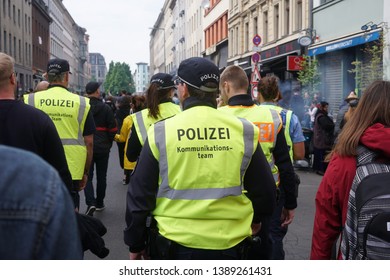 Berlin, Germany - May 1, 2019: Back Turned Policeman Wearing The Yellow Bib Of The Communication Team (German: Kommunikationsteams), Anti-conflict Group Of The German Police