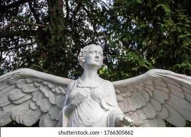 Berlin, Germany - May 6, 2016: Marble Statue Of An Angel Standing In The Middle Of A Cemetery Park With Green Trees.